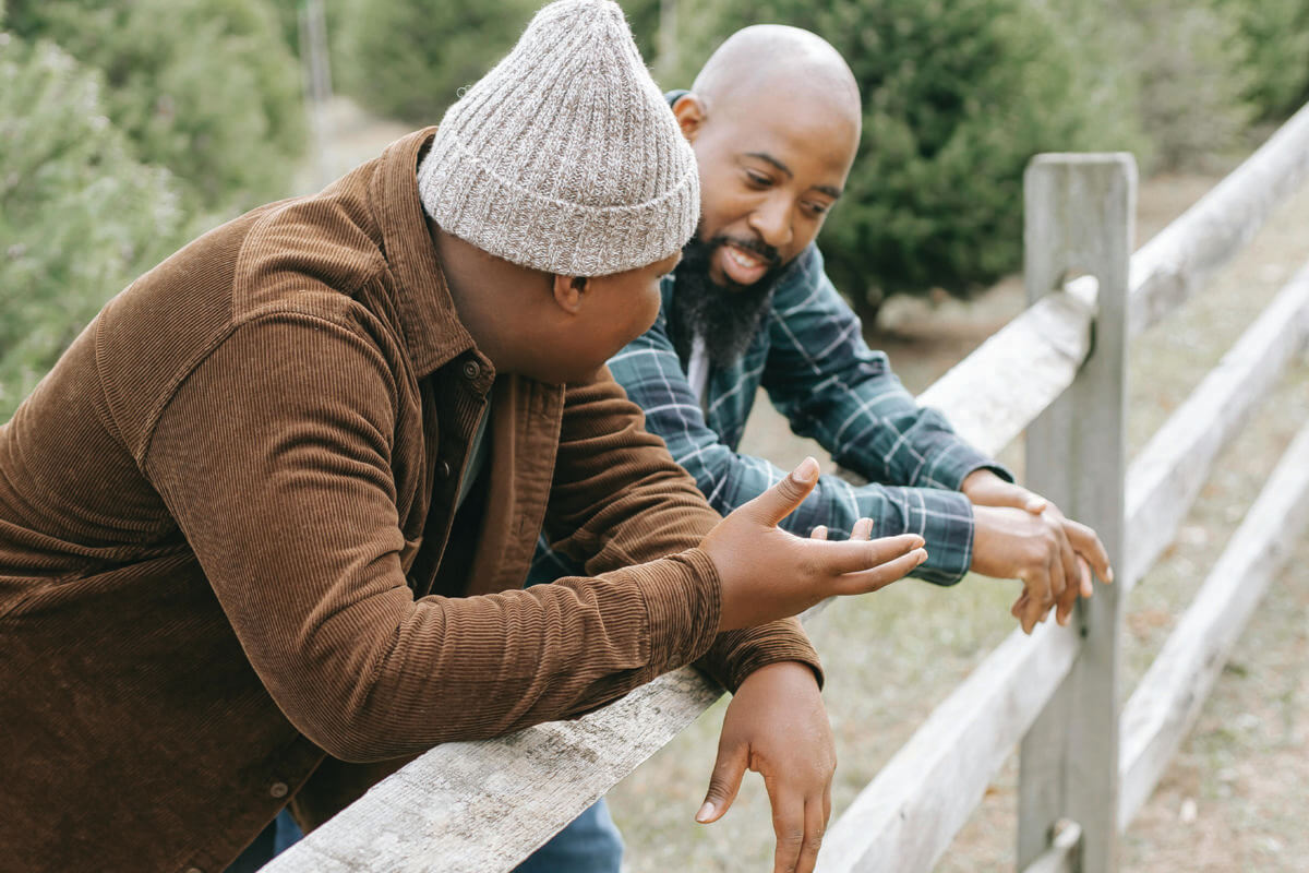 Young man and his father talking outside near a fence
